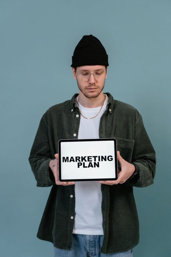 Top 10 SEO Strategies to Rank Higher on Google Adult wearing casual clothing holding a tablet that reads 'Marketing Plan'.