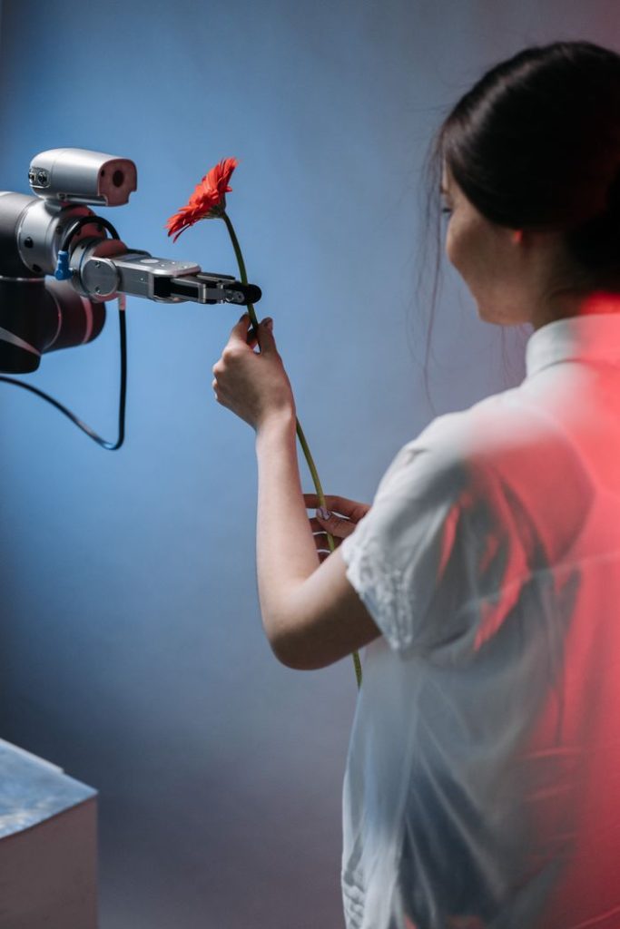 AI Used by Humans:1 How Artificial Intelligence Is Changing Everyday Life A robotic arm delicately holds a red flower as a woman interacts with it.